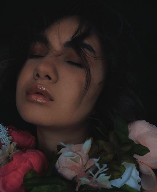 A peaceful portrait of a woman with eyes closed, surrounded by vibrant florals, exuding tranquility.