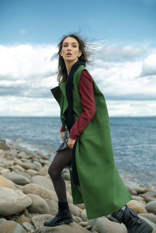 Woman in Green Coat Standing on Rocky Shore