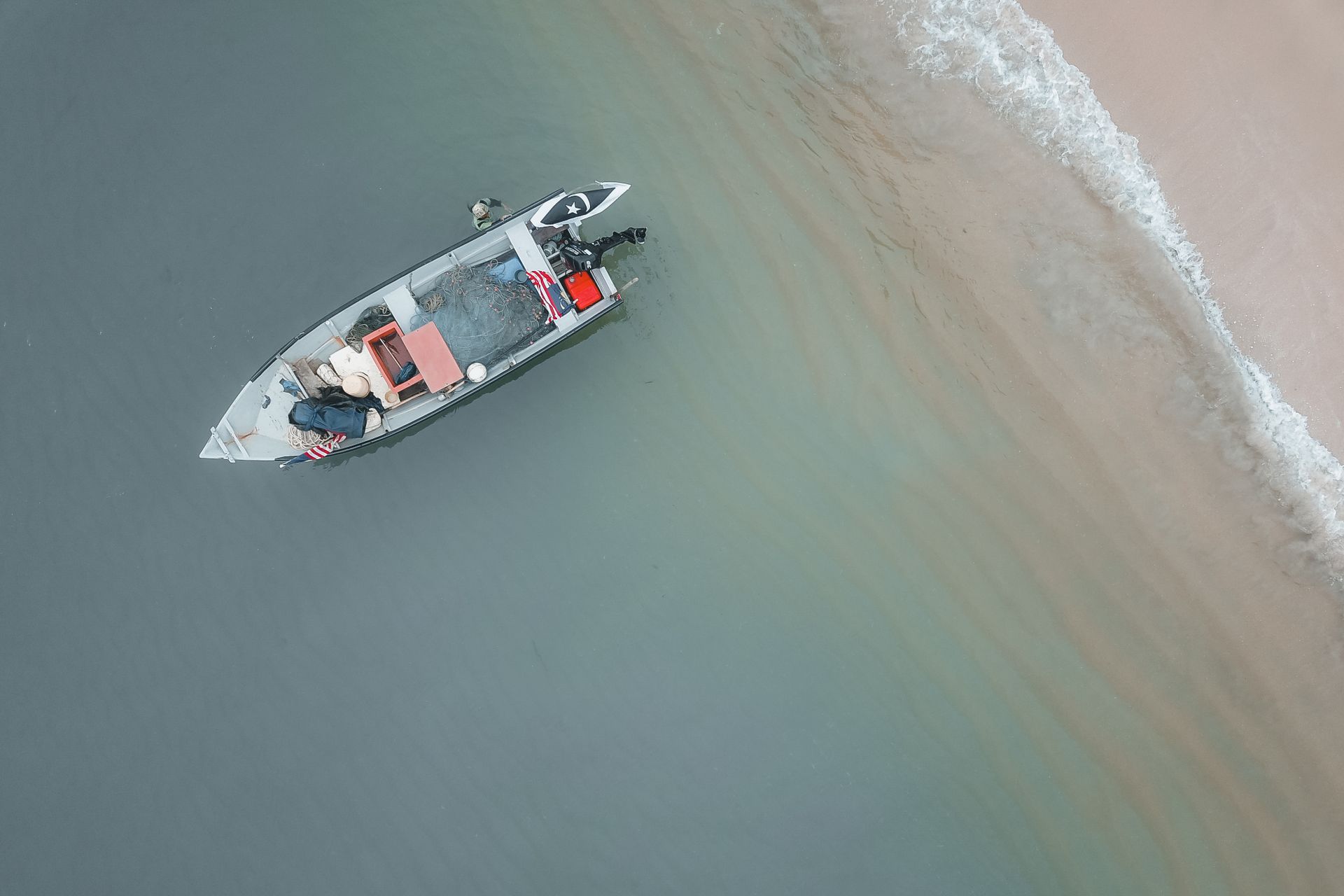 Aerial shot of a small fishing boat near a sandy beach shoreline with calm waters.