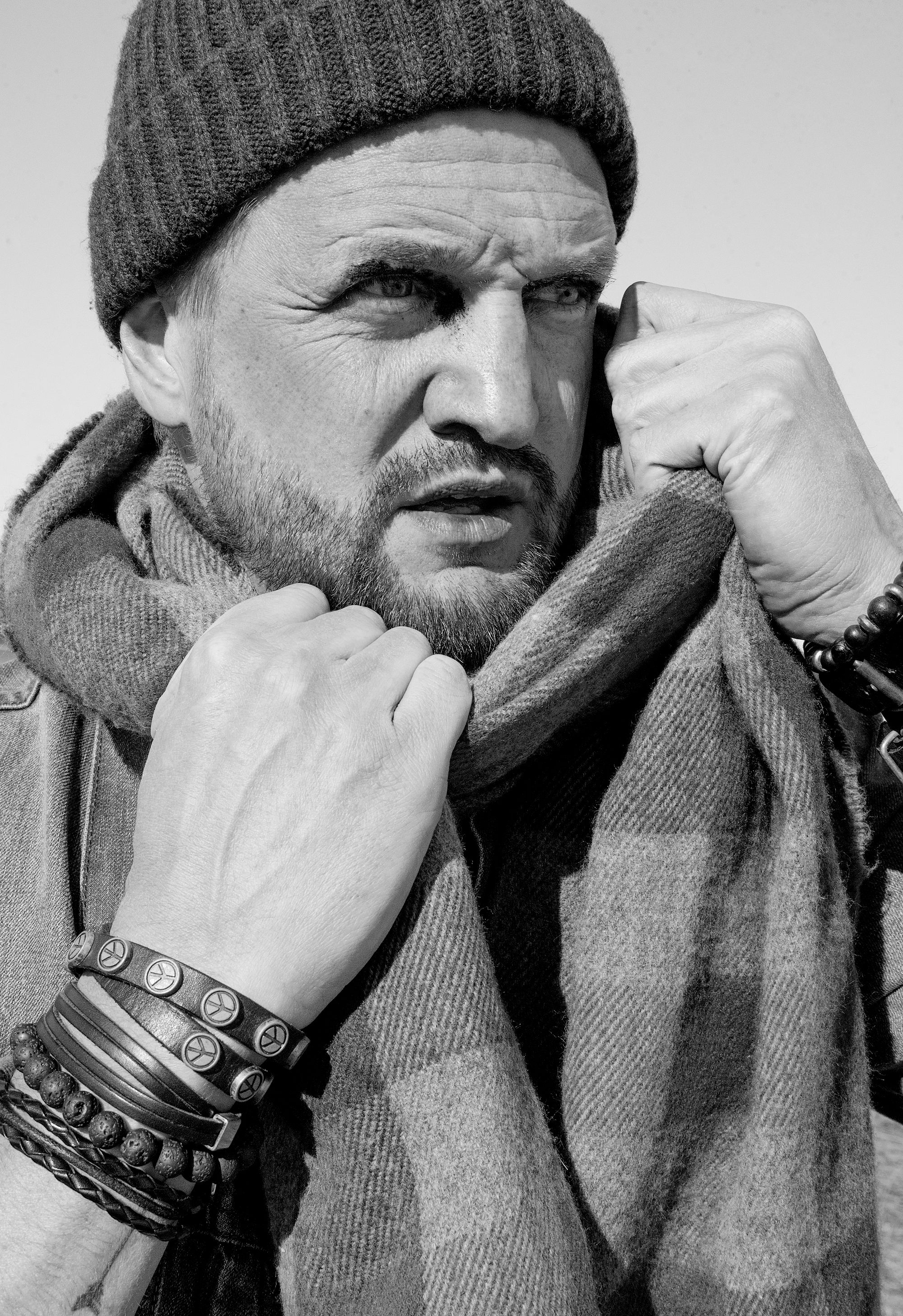 Black and white close-up of a bearded man wearing a beanie and scarf, exuding a pensive mood.