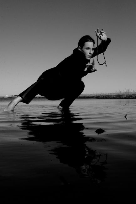 Striking monochrome portrait of a person crouching near the water, captured in a dramatic pose.