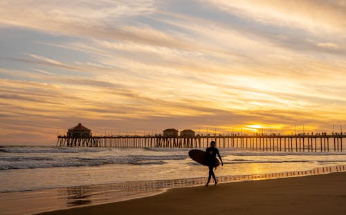 Silhouette of a Person Holding a Surfboard on the Beach