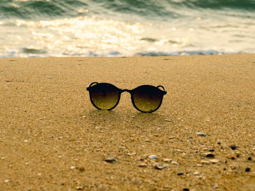 Close-Up Photo of Black Framed Sunglasses on Brown Sand