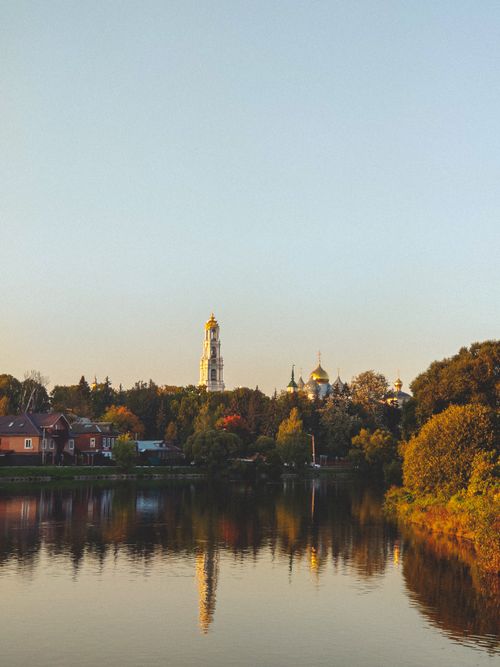Free Peaceful waterfront scene with a tranquil lake reflecting historic buildings and a tower at dusk. Stock Photo