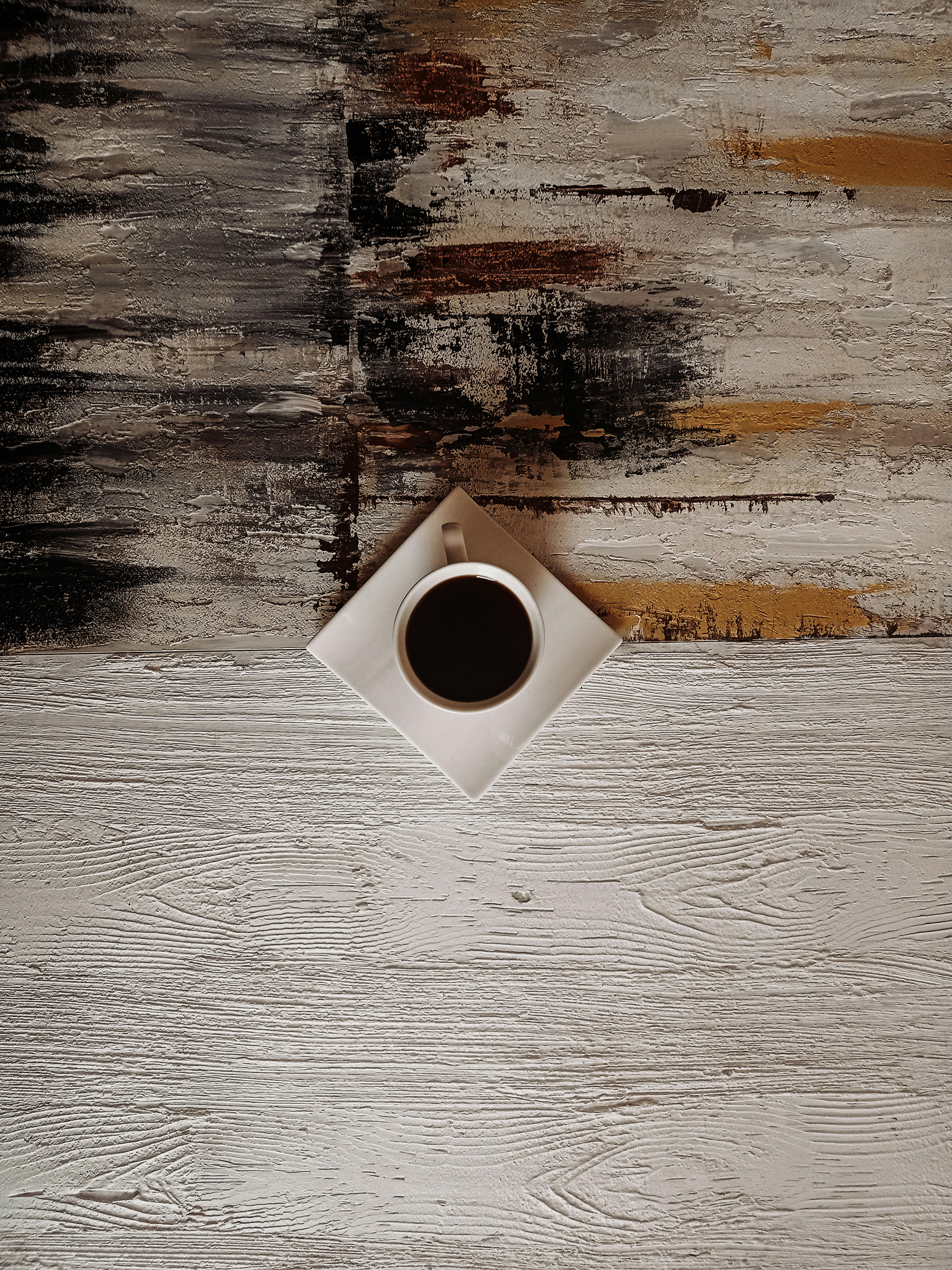 Minimalist coffee cup on a wooden and textured background, captured from above.