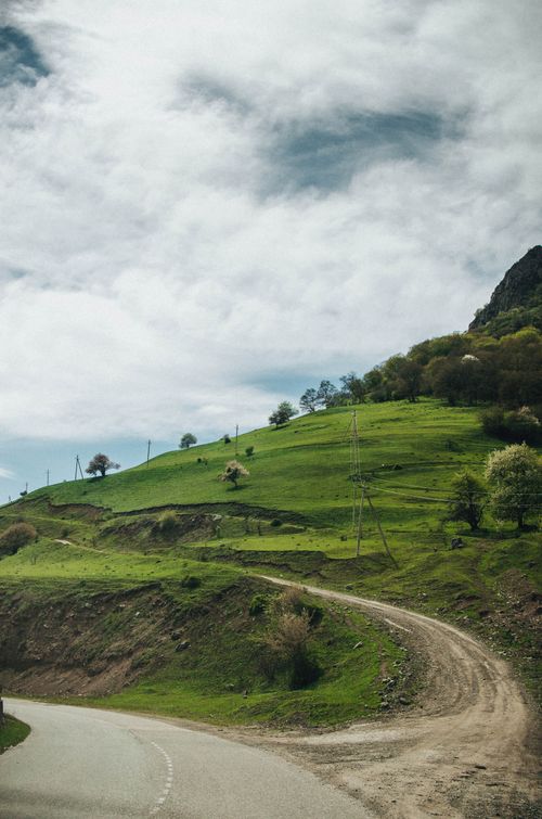 Free Curving dirt road through lush green hills in the Russian countryside under a cloudy sky. Stock Photo