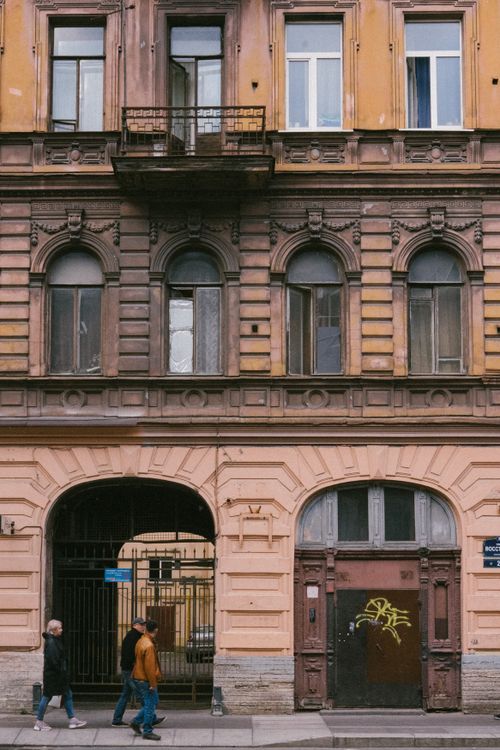 Free A vintage architectural facade in Saint Petersburg with arched windows and people walking by. Stock Photo