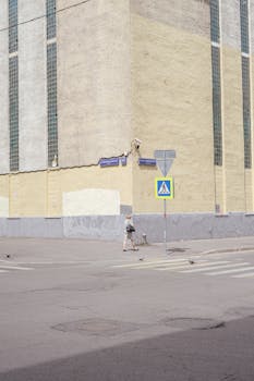 A woman walks along a Moscow street corner with a prominent pedestrian sign and urban architecture.