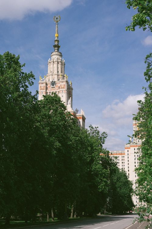 Free View of the Lomonosov Moscow State University tower framed by lush trees under a clear blue sky. Stock Photo