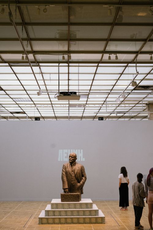 Free Visitors observe a statue of Lenin in a modern Moscow museum exhibit. Stock Photo