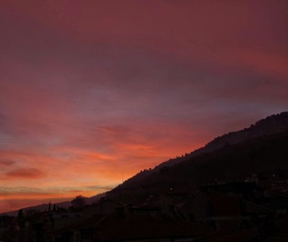 Captivating sunset with vibrant colors over silhouetted hills and urban landscape.