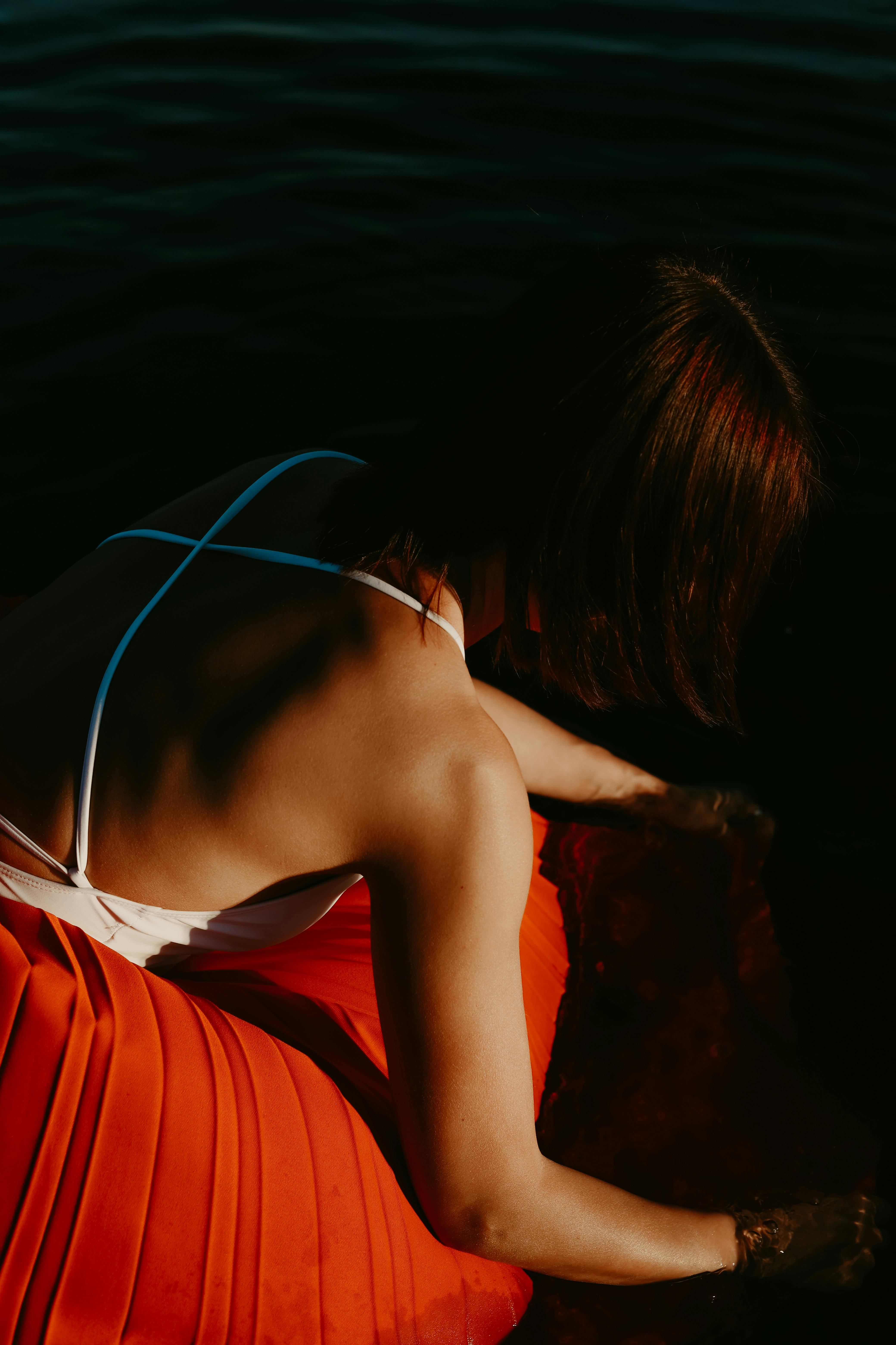 Woman in a backless dress by the water, capturing a dramatic blend of shadows and light.