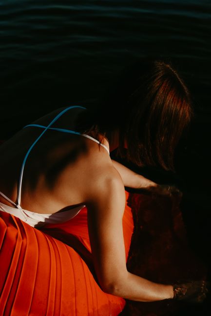 Woman in a backless dress by the water, capturing a dramatic blend of shadows and light.