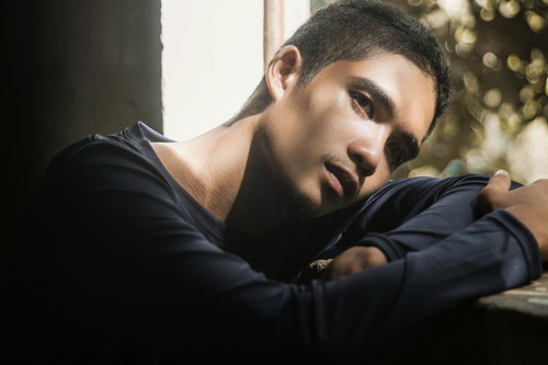 Free Close-up portrait of a thoughtful man sitting indoors with dramatic lighting. Stock Photo