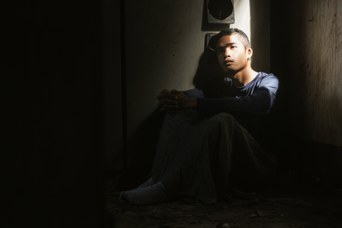 Free A young man sits alone in a dimly lit room, deep in thought. Stock Photo