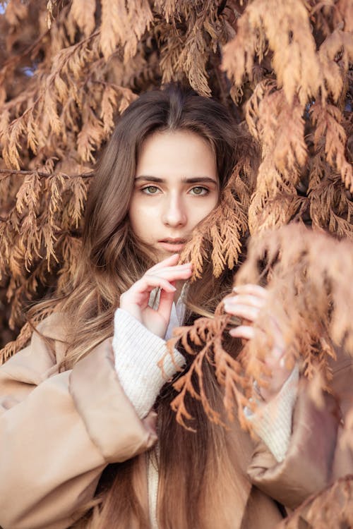 Woman in Beige Coat Surrounded by Dried Leaves