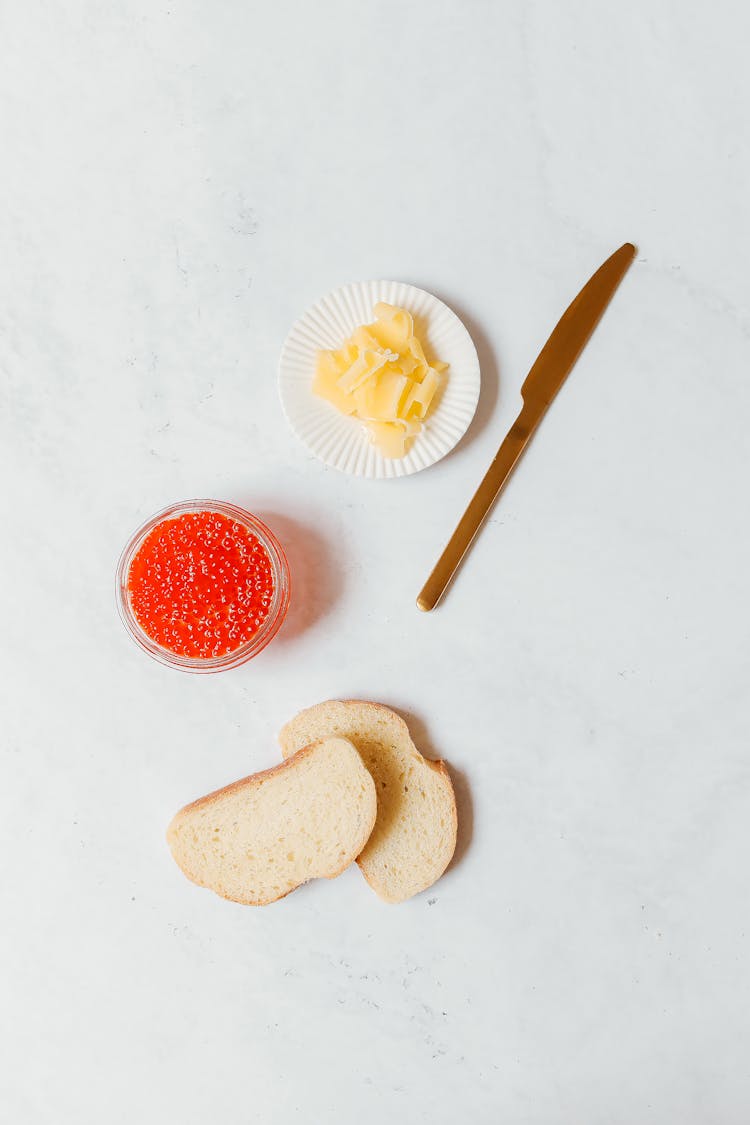 A Sliced Bread And Butter With Caviar On A White Surface