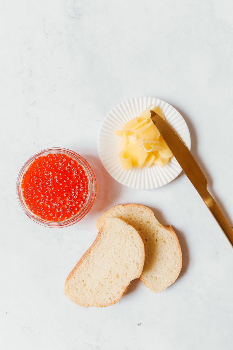 A Sliced Bread And Butter With Caviar On A White Surface