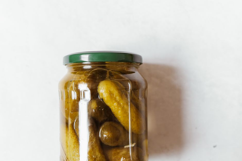 Close-up of a glass jar filled with pickles on a white surface.
