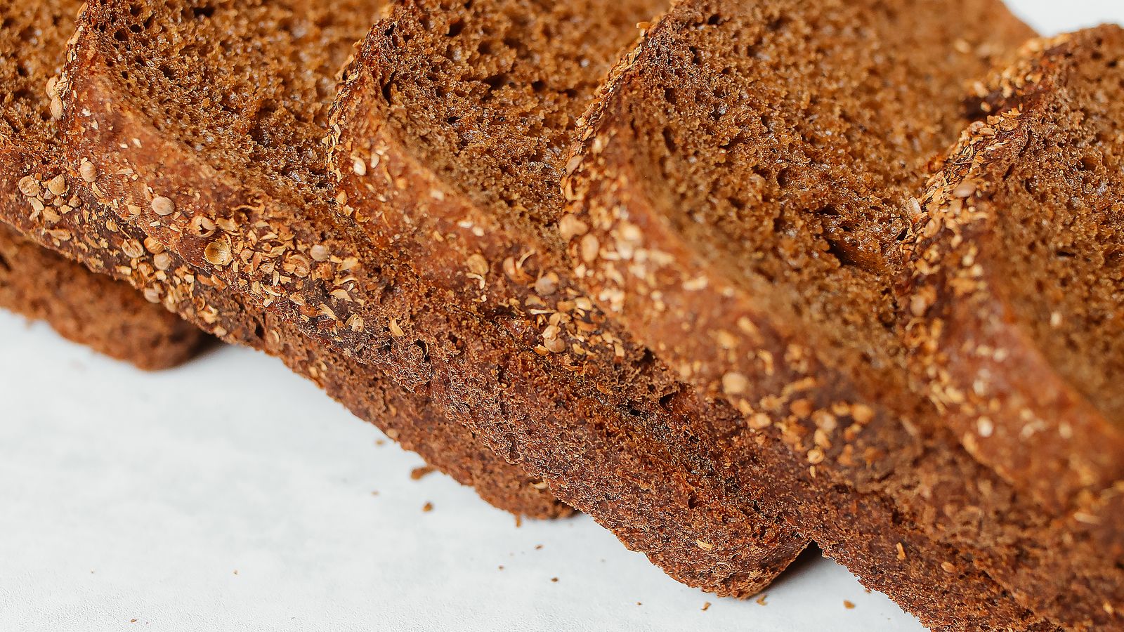 Sliced dark rye bread with seeds on a white surface — photo by Polina Tankilevitch on Pexels Sliced dark rye bread with seeds on a white surface