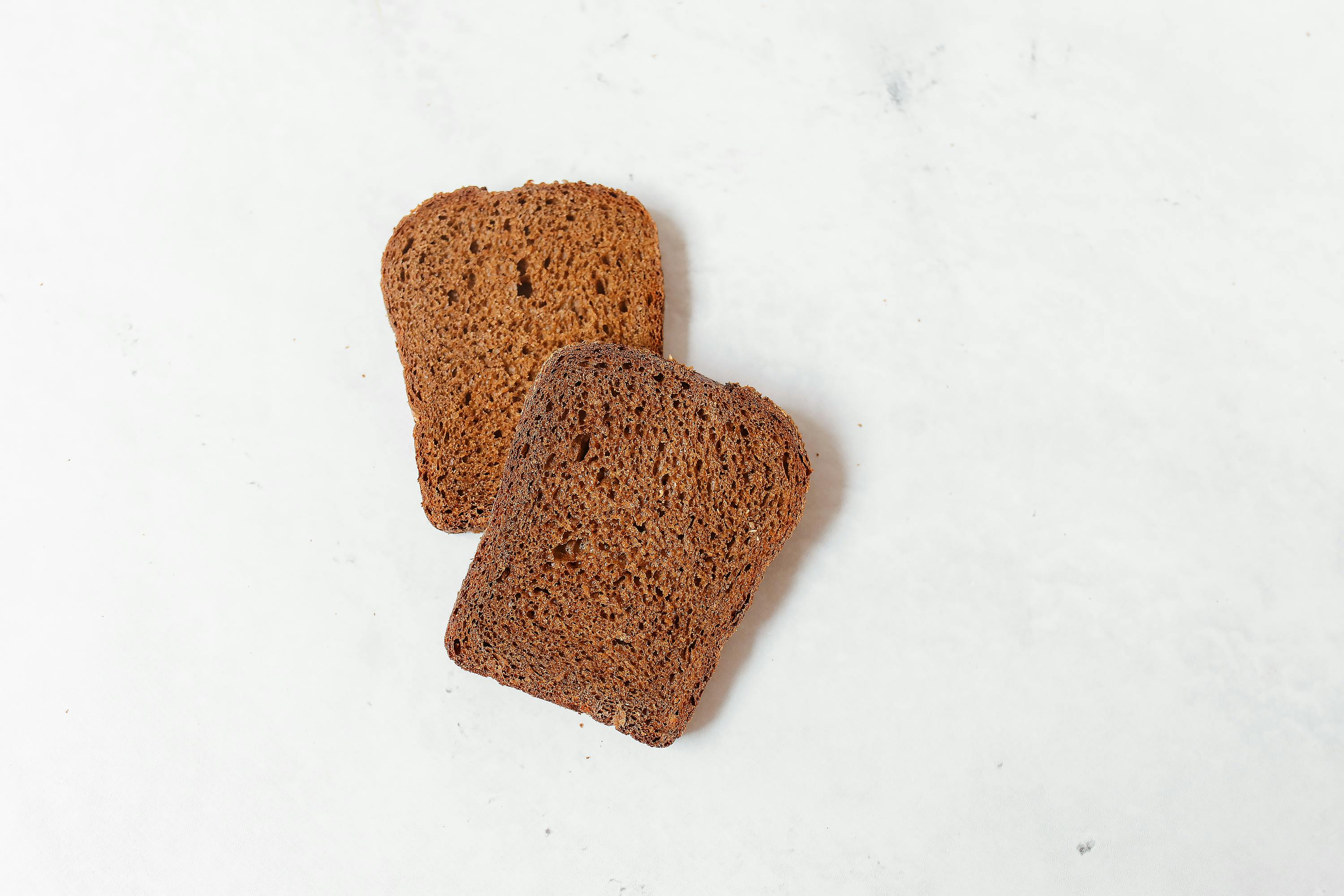 Close-up shot of two slices of dark rye bread on a white background, perfect for food blogs and culinary projects.