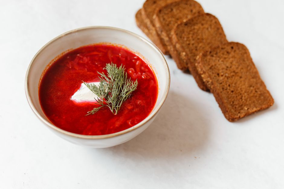 Vibrant bowl of borscht garnished with dill and served with slices of rye bread.
