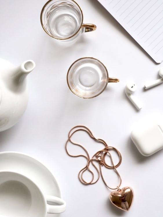 Gold-colored Heart Pendant Necklace Beside Two Glass Mugs on Table