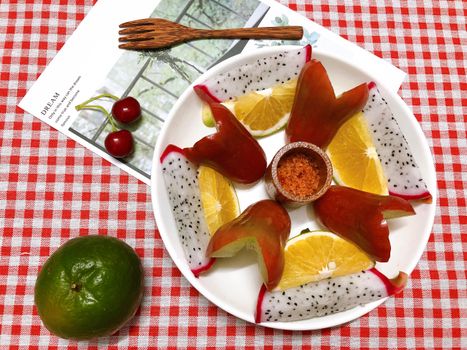 Vibrant fruit platter with oranges, dragon fruit, and cherries on a red checkered tablecloth.