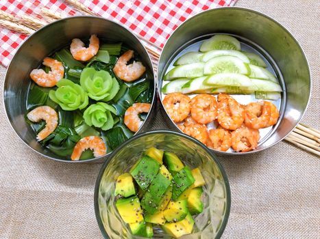 Fresh and healthy Asian meal featuring shrimp, avocado, cucumber, and leafy greens in bowls.