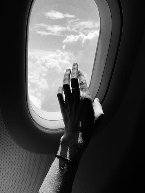 Grayscale Photo of a Person's Hand near the Airplane Window