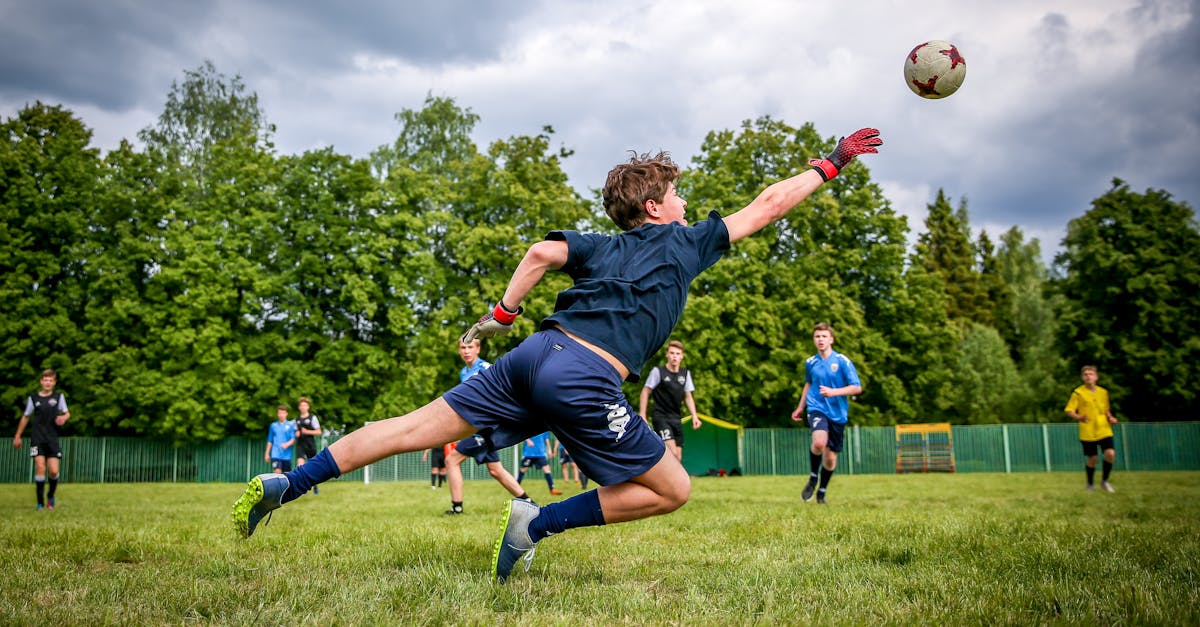 A young goalkeeper dives to catch a soccer ball during a lively outdoor game on a green field.