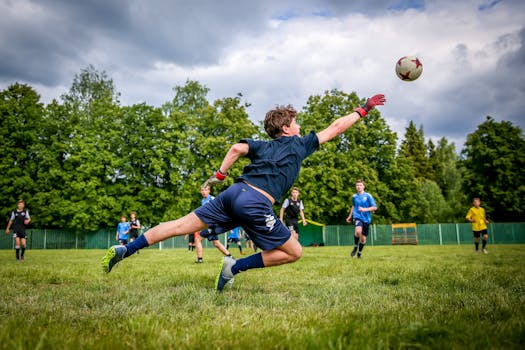 A young goalkeeper dives to catch a soccer ball during a lively outdoor game on a green field.