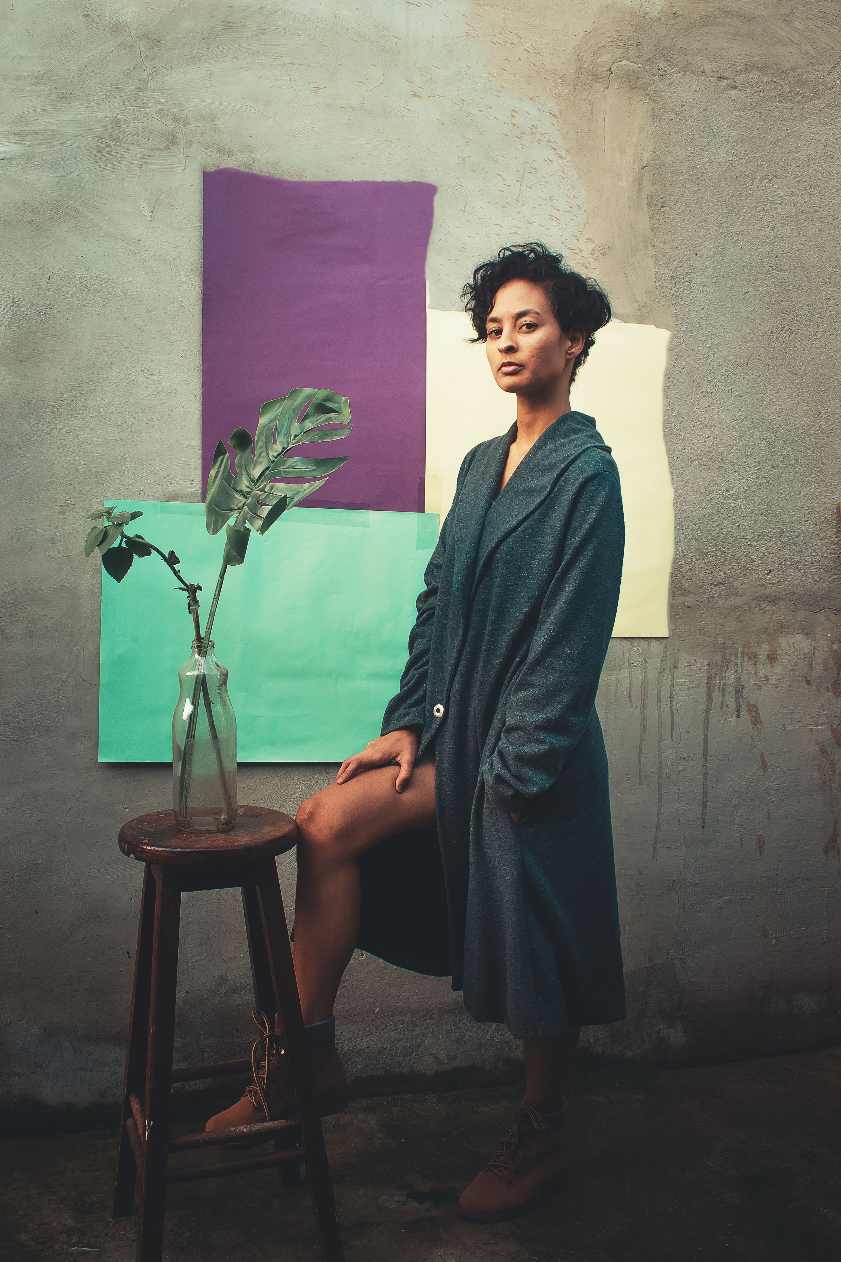 Elegant woman posing in a teal coat with a creative and colorful artistic background.