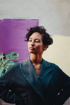 Confident woman with short curly hair in a stylish gray jacket against a colorful backdrop.