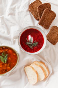 A delicious flatlay of traditional borscht soup, rye and white bread slices on a rustic cloth.