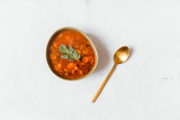 A Delicious Bowl Of Soup With  Dried Leaves And A Gold Spoon