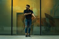 Man in Black Polo and Ripped Jeans Posing near a Glass