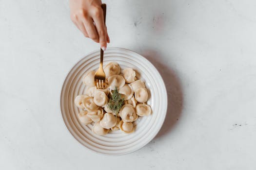Top view of a plate of Russian pelmeni with a hand holding a fork, showcasing traditional cuisine.