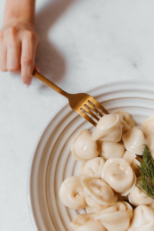 Free A hand holding a fork poised over fresh dumplings on a white plate, showcasing food elegance. Stock Photo