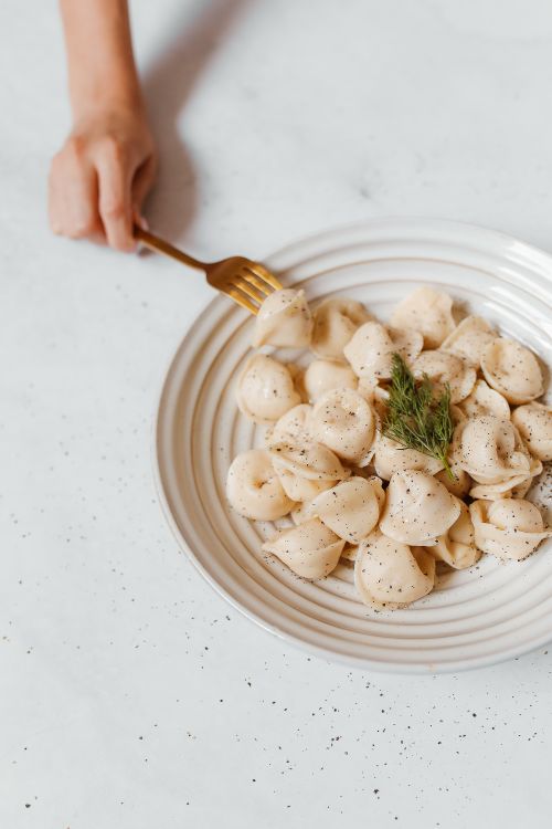 Free Hand holding fork with tasty Russian dumplings on a ceramic plate, garnished with dill. Stock Photo