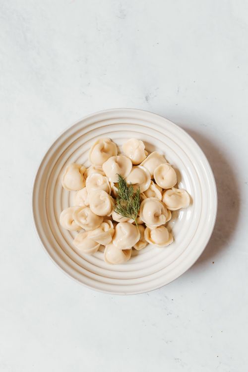 Free Flat lay of delicious Russian pelmeni dumplings on a white ceramic plate with dill garnish. Stock Photo