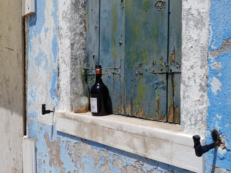 Empty Bottles Of Alcohol Standing On Windowsill Of Old House