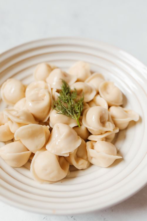 Free Tasty Russian pelmeni dumplings on a ceramic plate with dill garnish on a white surface. Stock Photo
