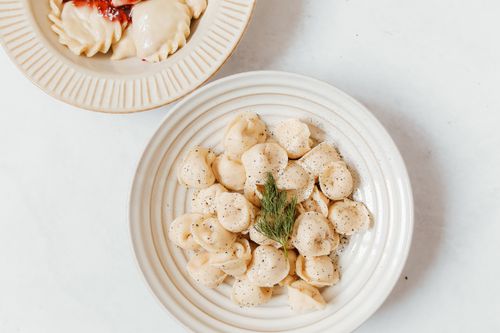 Free Close-up of Russian dumplings on ceramic plates garnished with dill, on a white surface. Stock Photo