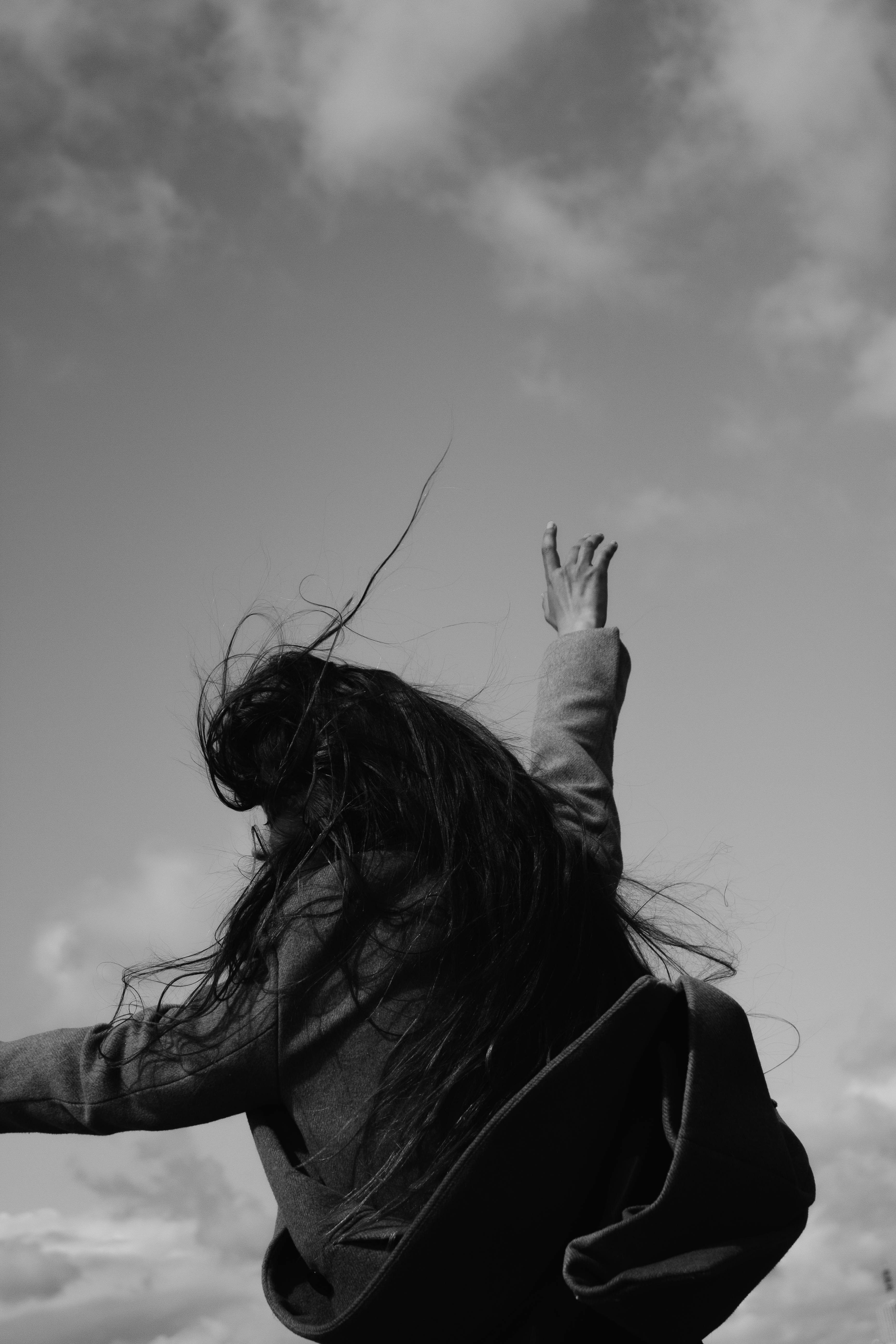 Black and white photo of a woman with long hair reaching towards the sky, conveying a sense of freedom.