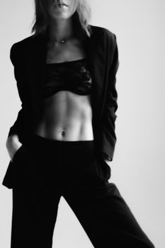 Elegant black and white portrait of a person in a blazer posing confidently in a studio.