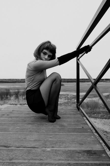 Black and white photo of a stylish woman posing with a modern railing on a wooden bridge.