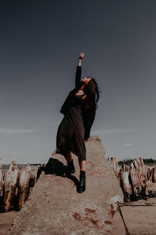 Woman in Black Clothes Raising her Hand Standing on a Rock