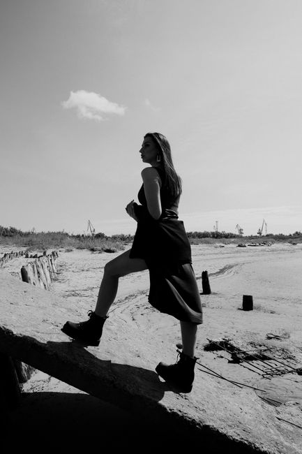 Monochrome shot of a woman standing on a rock outdoors with a clear sky.