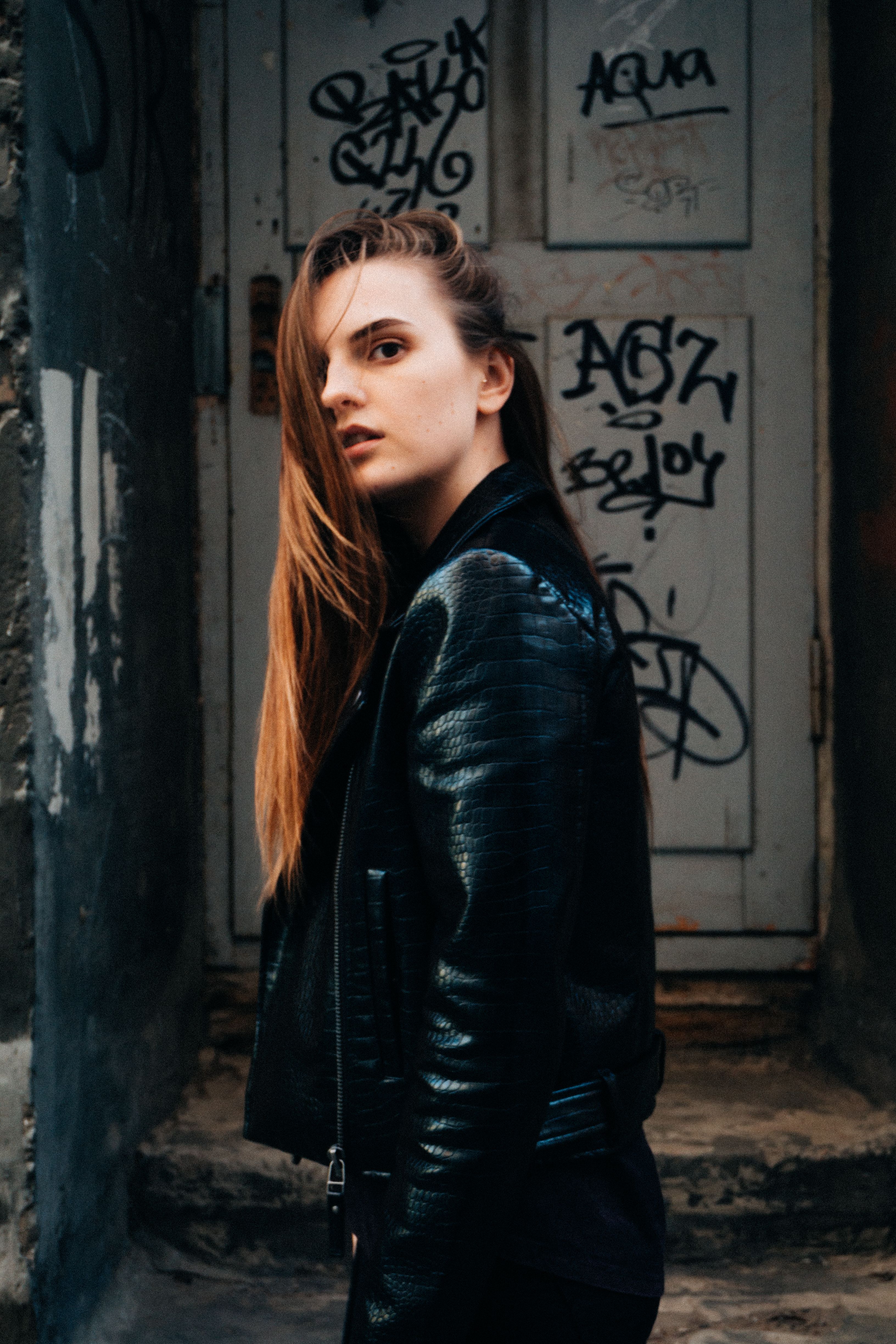 Woman in Black Leather Jacket Standing Beside Gray Wall · Free Stock Photo